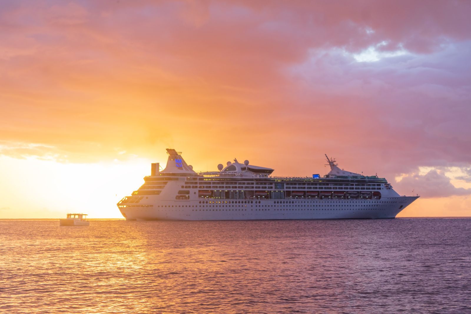 A cruise ship at sea under an orange and pink sunset sky