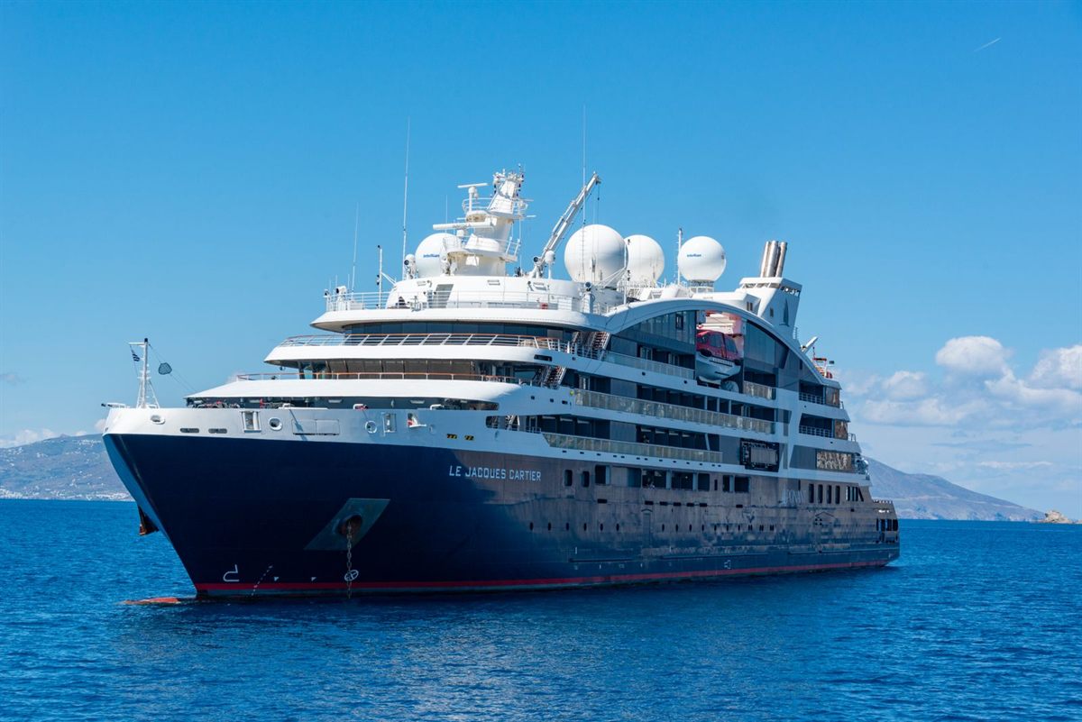 A small expedition-style cruise ship with a dark hull at anchor in a deep blue bay