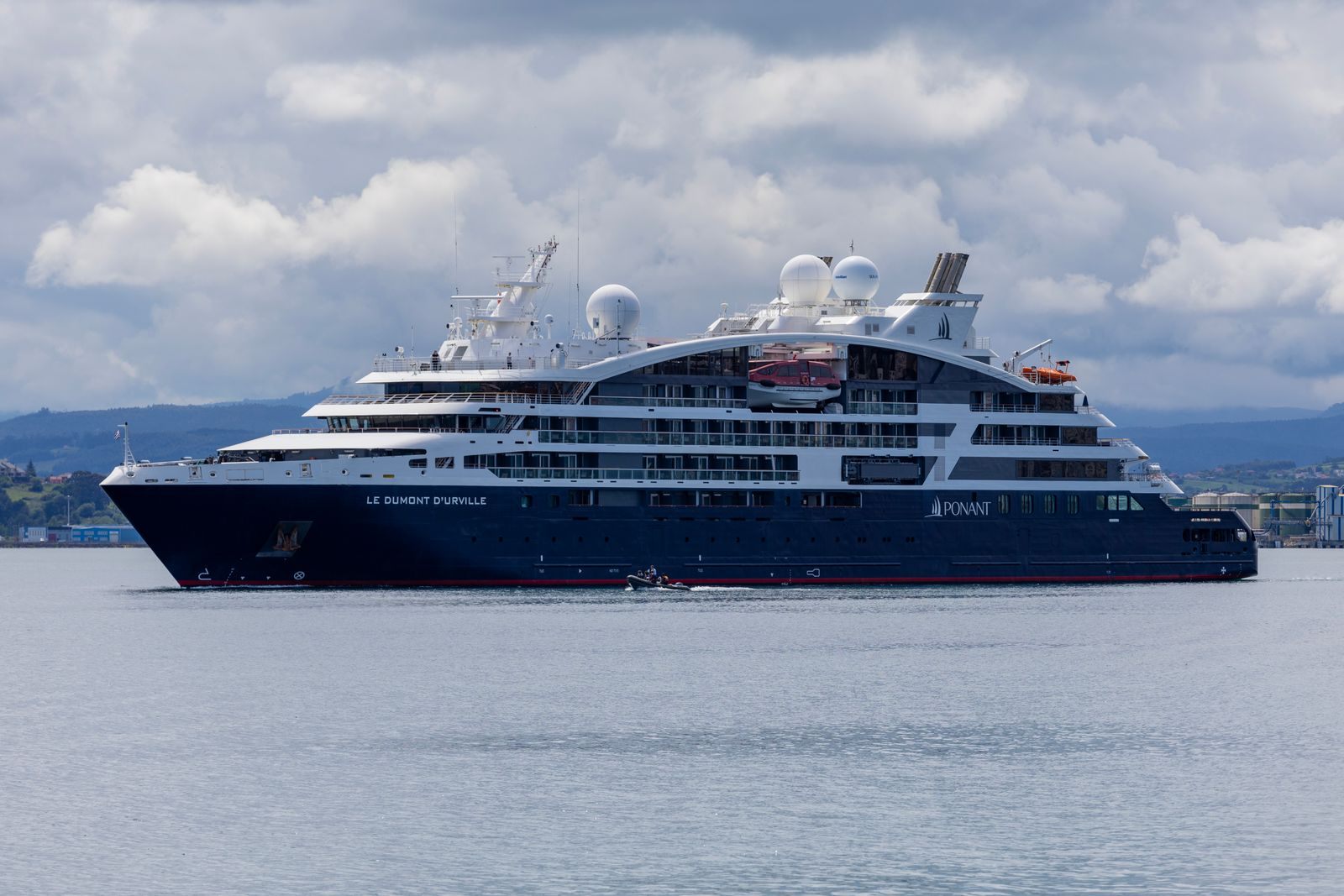 A small expedition cruise ship anchored offshore, one of the ship styles luxury cruise companies offer
