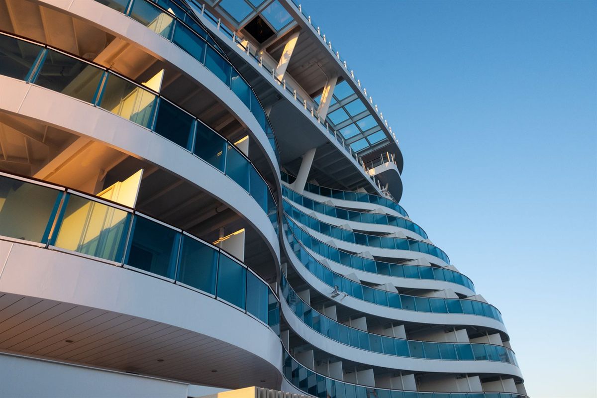 Curved tiers of cruise ship balconies against a clear blue sky