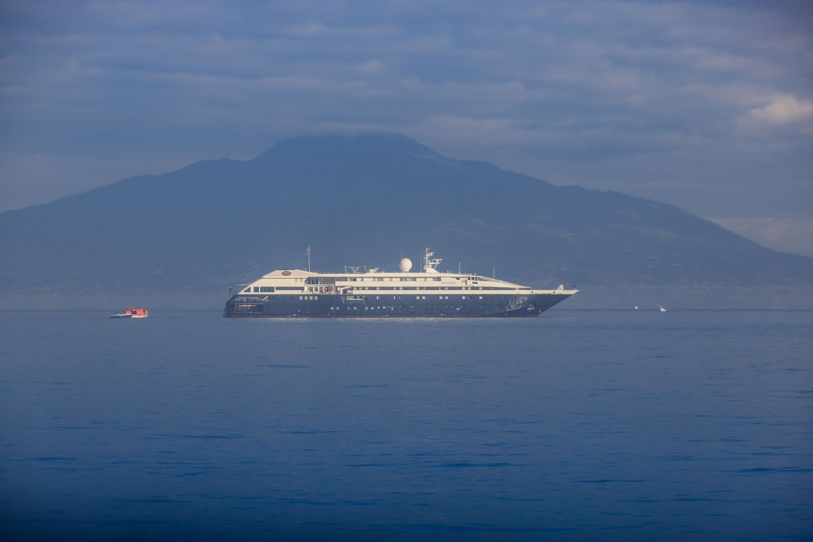 A small luxury cruise ship in a calm bay beneath a mountain at dusk, a sailing a luxury cruise advisor might recommend